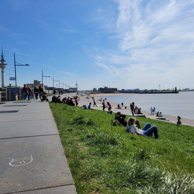 Menschen flanieren und entspannen auf der sonnigen Deichpromenade am Wasser in Bremerhaven.