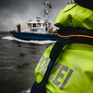 Person mit Schutzweste und Aufschrift Polizei auf einem Boot
