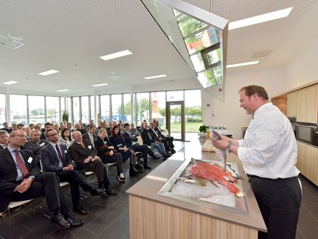 Koch demonstriert in moderner Küche die Zubereitung frischen Fisches vor aufmerksamem Publikum.