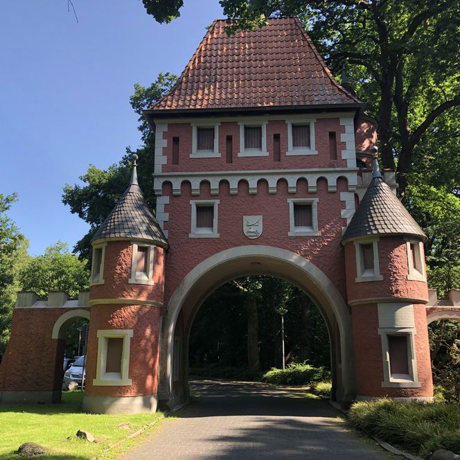 Historisches Torhaus aus rotem Backstein mit spitzen Türmen, umgeben von grünen Bäumen im Gesundheitspark Speckenbüttel Bremerhaven.