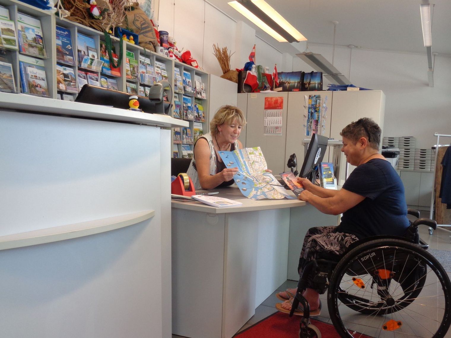 Ein Frau im Rollstuhl wird in der Tourist-Info bedient