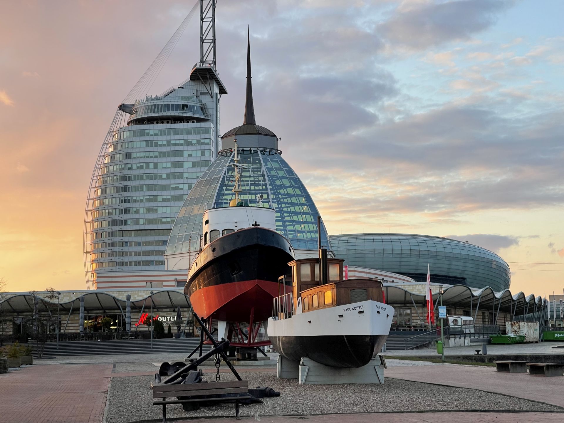 Zwei historische Schiffe vor moderner Architektur im Museumshafen Bremerhaven bei Abendlicht.